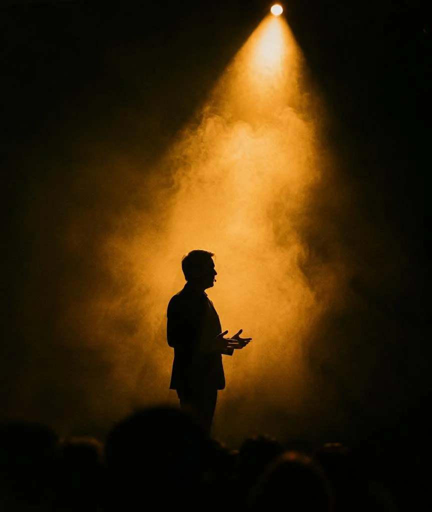 Speaker silhouetted on stage under a gold spotlight